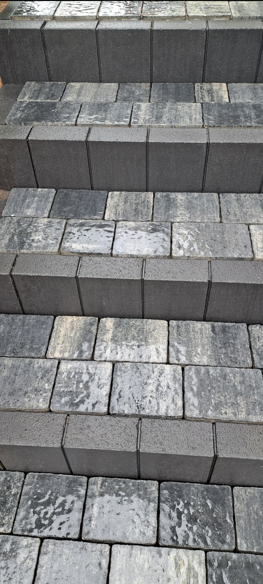 Schody zewnętrzne wykonane z ciemnoszarej kostki brukowej, widoczne z dołu, z delikatnym połyskiem od wilgoci.