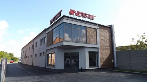 Dwukondygnacyjny budynek biurowy z szarą fasadą i drewnianym akcentem, z logo 'NORMET' na dachu.