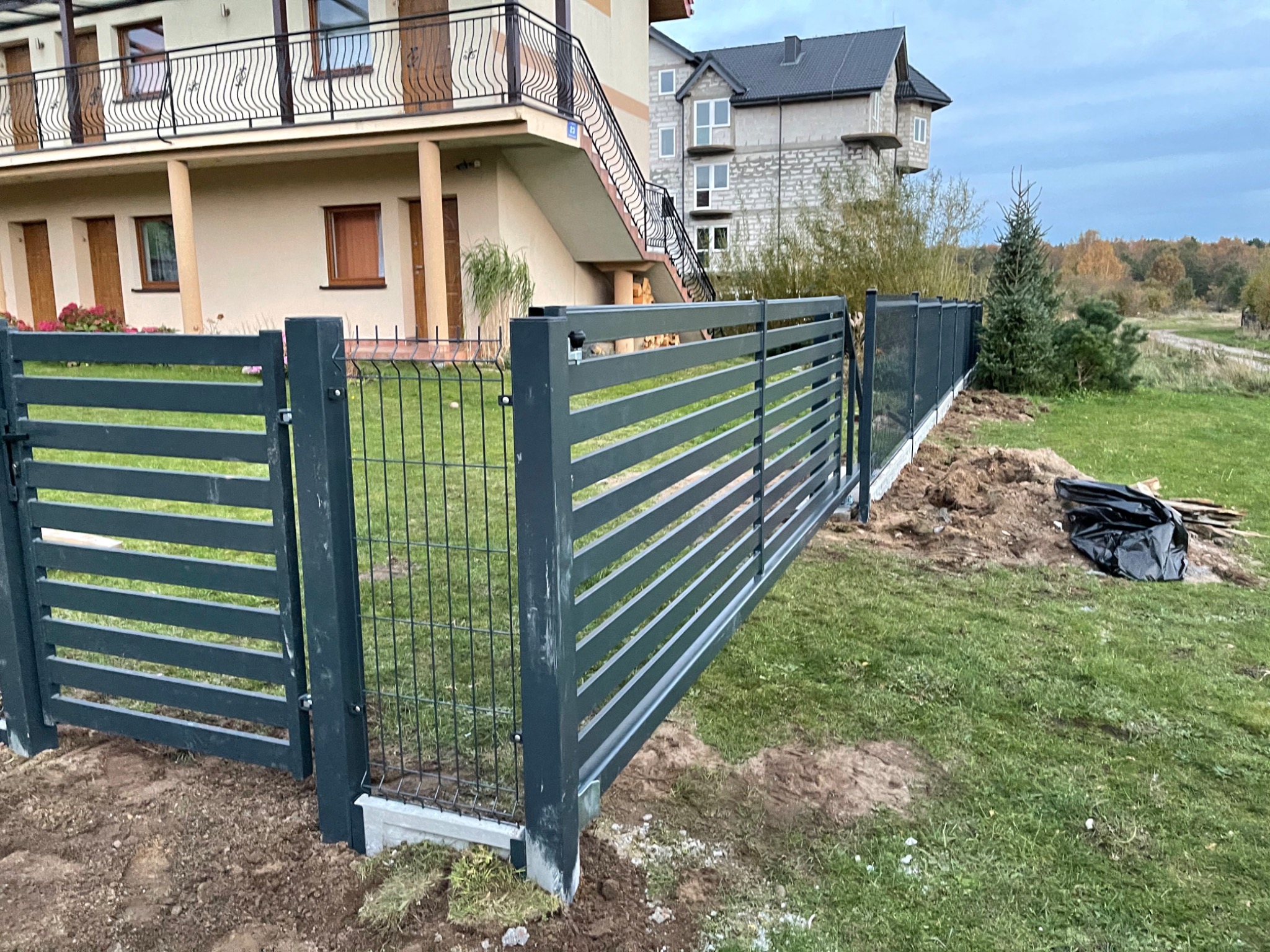 Nowoczesne, poziome ogrodzenie panelowe w kolorze grafitowym z bramą wjazdową, świeżo zamontowane w Szczecinku, widoczne ślady prac ziemnych wokół słupków.