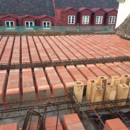 Układanie stropu z pustaków ceramicznych na zbrojeniu stalowym, widoczne drewniane szalunki, w tle czerwony dach z lukarnami.