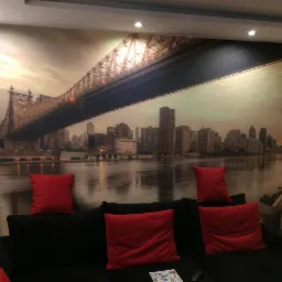 Fototapeta z widokiem na most i panoramę miasta za czarną sofą z czerwonymi poduszkami w salonie.