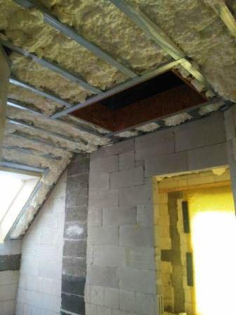 Ocieplanie poddasza pianką PUR z widoczną konstrukcją metalową i niezabezpieczonym otworem w stropie.