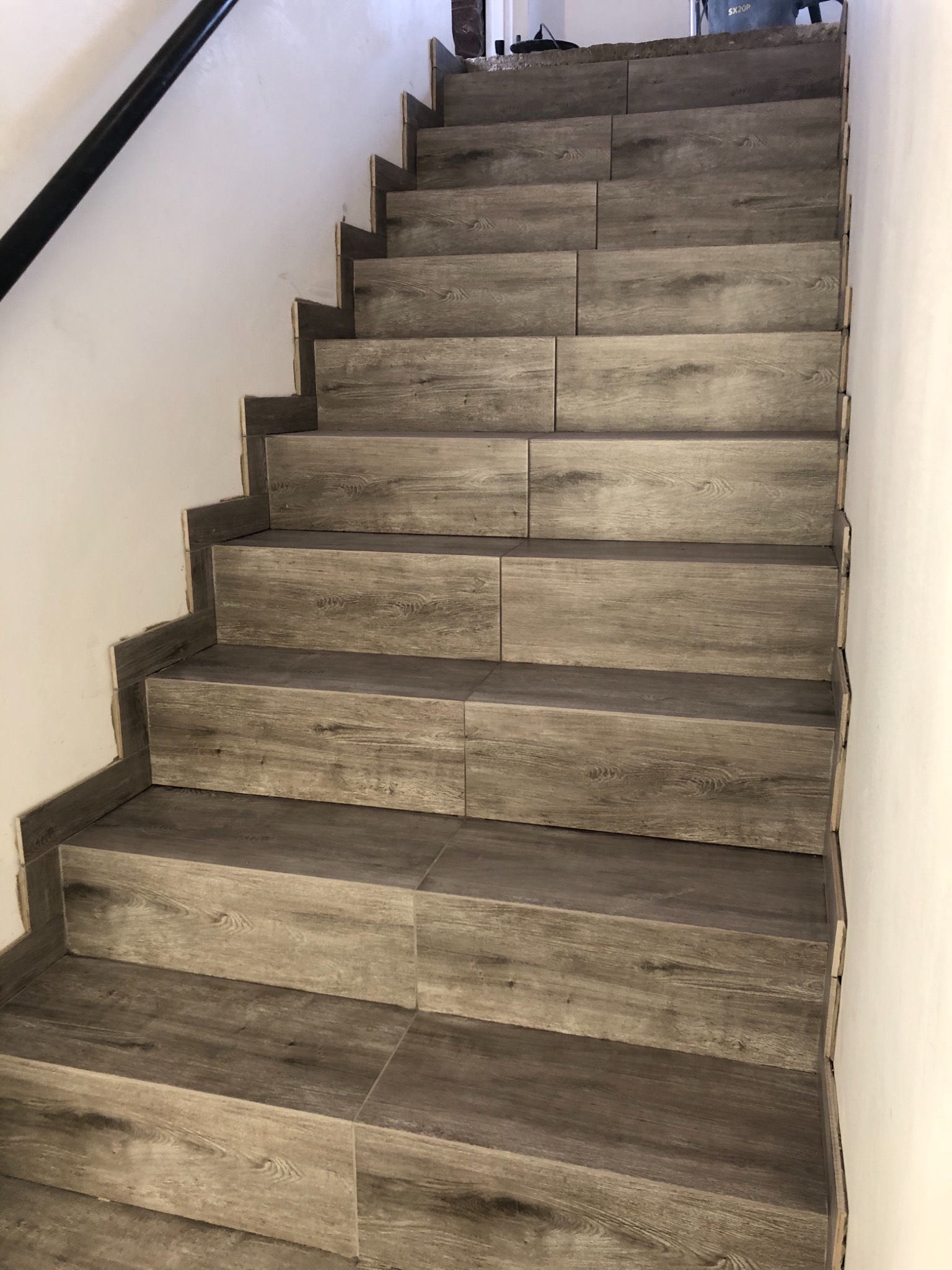 Schody wyłożone płytkami imitującymi drewno, widoczne niedokończone wykończenia przy ścianie.