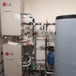 Dwa moduły pompy ciepła LG Therma V połączone rurami z instalacją grzewczą, w tle szary zasobnik ciepłej wody i niebieskie naczynie przeponowe.