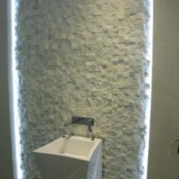 Nowoczesna łazienka z umywalką na postumencie i ścianą wyłożoną mozaiką z kamienia naturalnego, podświetloną pionowymi pasami LED po bokach.