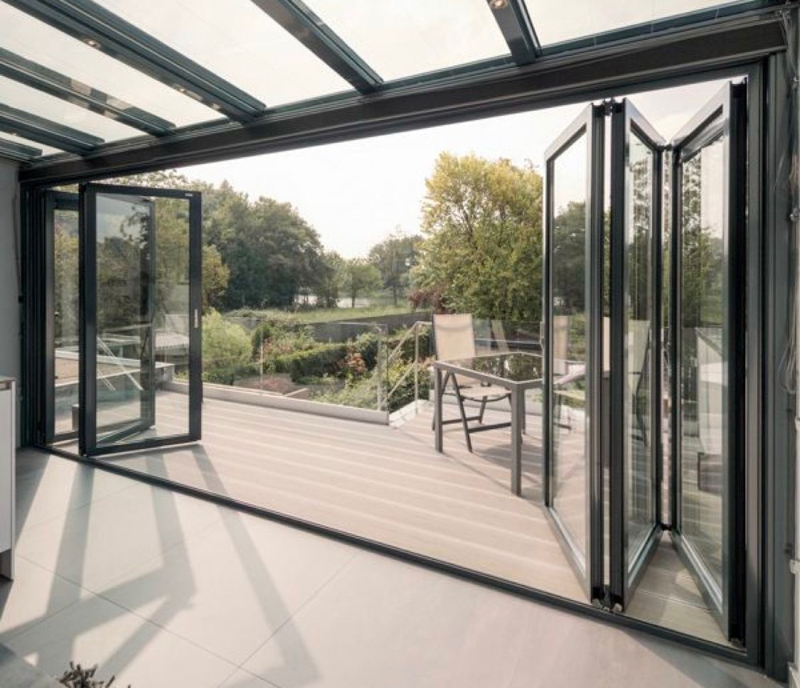 Nowoczesne, składane drzwi tarasowe z aluminiową ramą, otwarte na taras z widokiem na ogród i jezioro w tle.