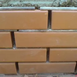 Fragment elewacji z klinkieru, widoczne ułożone cegły klinkierowe w rzędach, z szarą zaprawą pomiędzy nimi i pod górną warstwą cegieł.