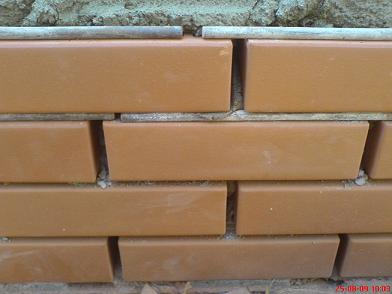 Fragment elewacji z klinkieru, widoczne ułożone cegły klinkierowe w rzędach, z szarą zaprawą pomiędzy nimi i pod górną warstwą cegieł.