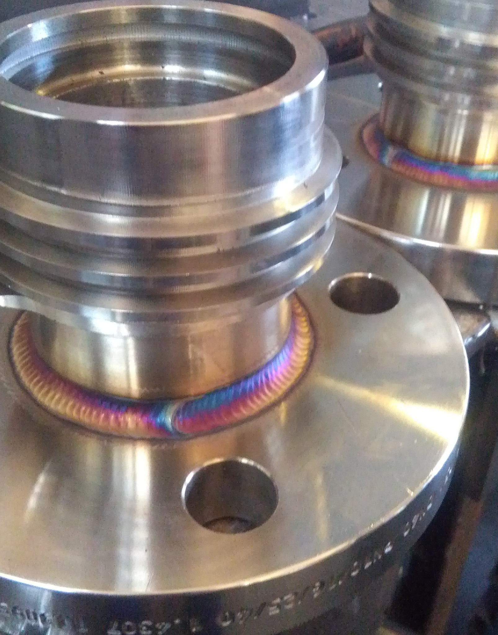 Dwa metalowe kołnierze połączone spoiną z widocznymi efektami termicznymi w postaci kolorowych przebarwień.