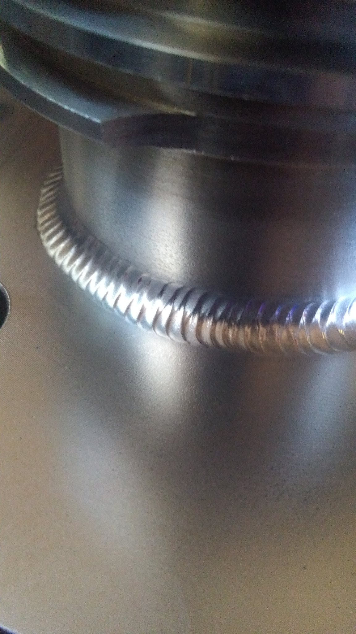 Szczegółowe zbliżenie na spawany szew łączący metalowe elementy, widoczne drobne nierówności i refleksy światła na spoinie.