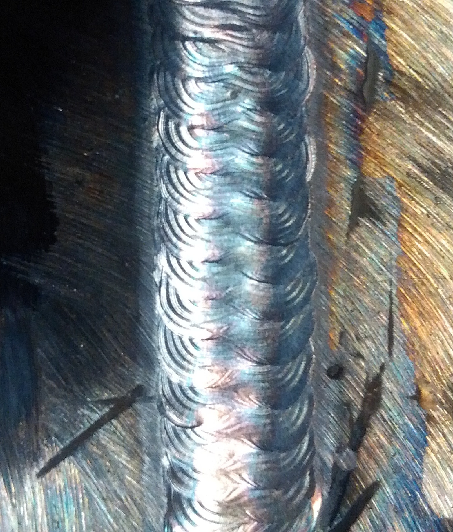 Szczegółowe ujęcie spoiny wykonanej w Ogrodzieńcu, ukazujące charakterystyczny wzór łusek i opalizujące przebarwienia termiczne na metalu.