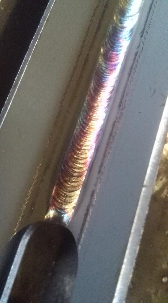 Spoina na metalowym profilu, widoczne tęczowe przebarwienia termiczne, zbliżenie na obszar łączenia.