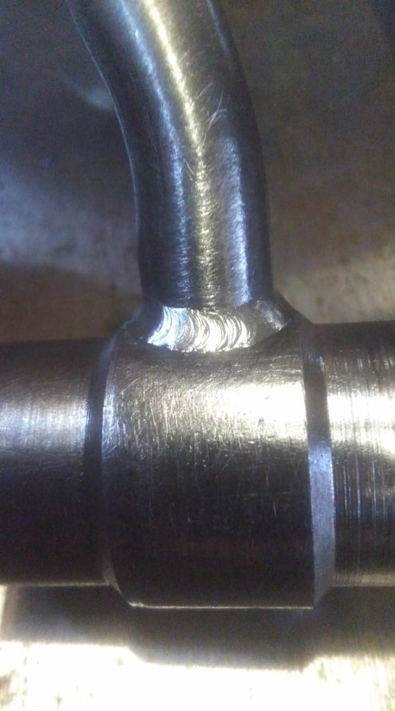 Spoina rury metalowej w kształcie litery T, widoczne ślady obróbki i zarysowania na powierzchni metalu.