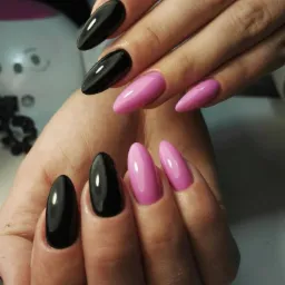 Dłonie z manicure hybrydowym: czarne, błyszczące paznokcie w kształcie migdała oraz różowe, owalne paznokcie. Widoczna lampa UV w tle.