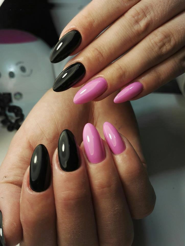 Dłonie z manicure hybrydowym: czarne, błyszczące paznokcie w kształcie migdała oraz różowe, owalne paznokcie. Widoczna lampa UV w tle.