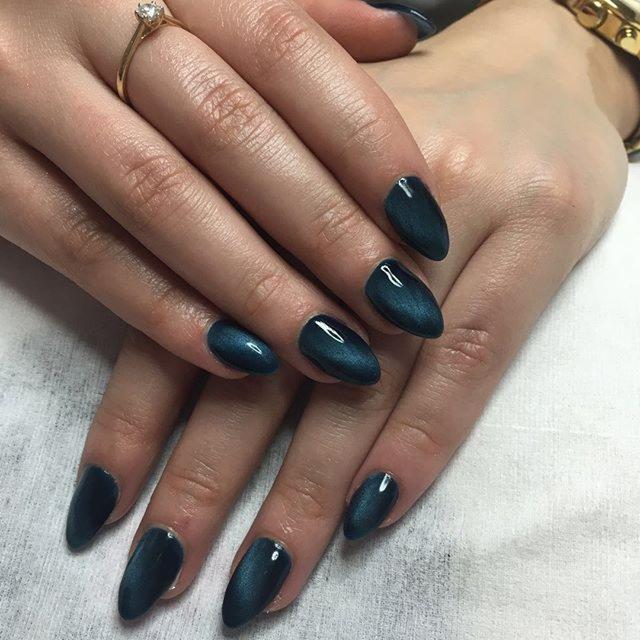 Dłonie z ciemnozielonym manicurem w stylu 'kocie oko', pierścionek z brylantem na palcu serdecznym i złoty zegarek na nadgarstku.