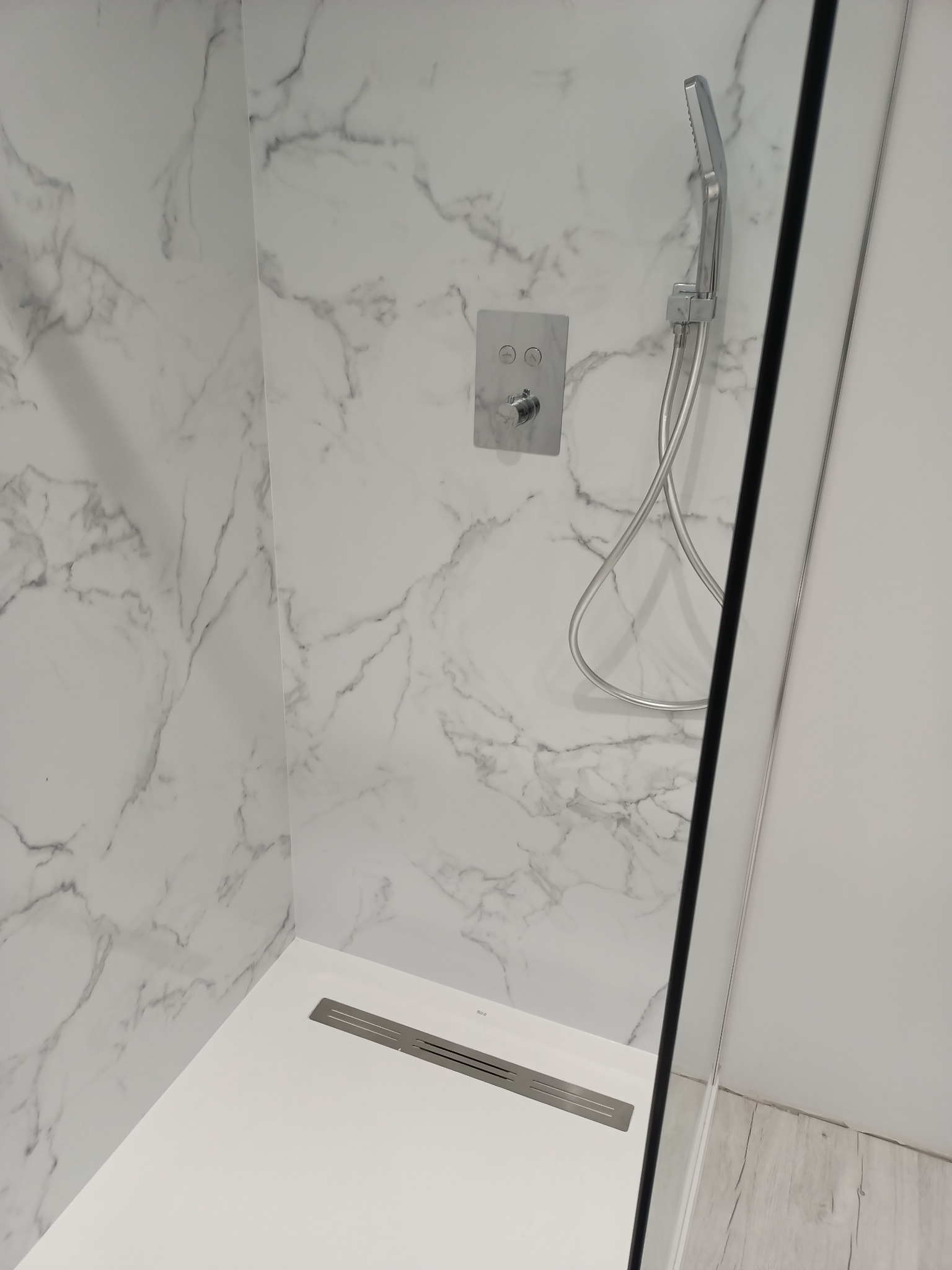 Nowoczesna kabina prysznicowa walk-in z marmurowymi płytami ściennymi, minimalistyczną armaturą i odpływem liniowym.