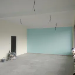 Wnętrze biura po świeżym malowaniu ścian na dwa kolory: kremowy i turkusowy, widoczne wystające kable, odkurzacz przemysłowy i resztki materiałów budowlanych przy oknie.