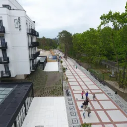 Widok z góry na nowo wybudowany budynek Baltic Park Forti z chodnikiem z kostki w kratkę, otoczony zielenią i spacerującymi ludźmi.