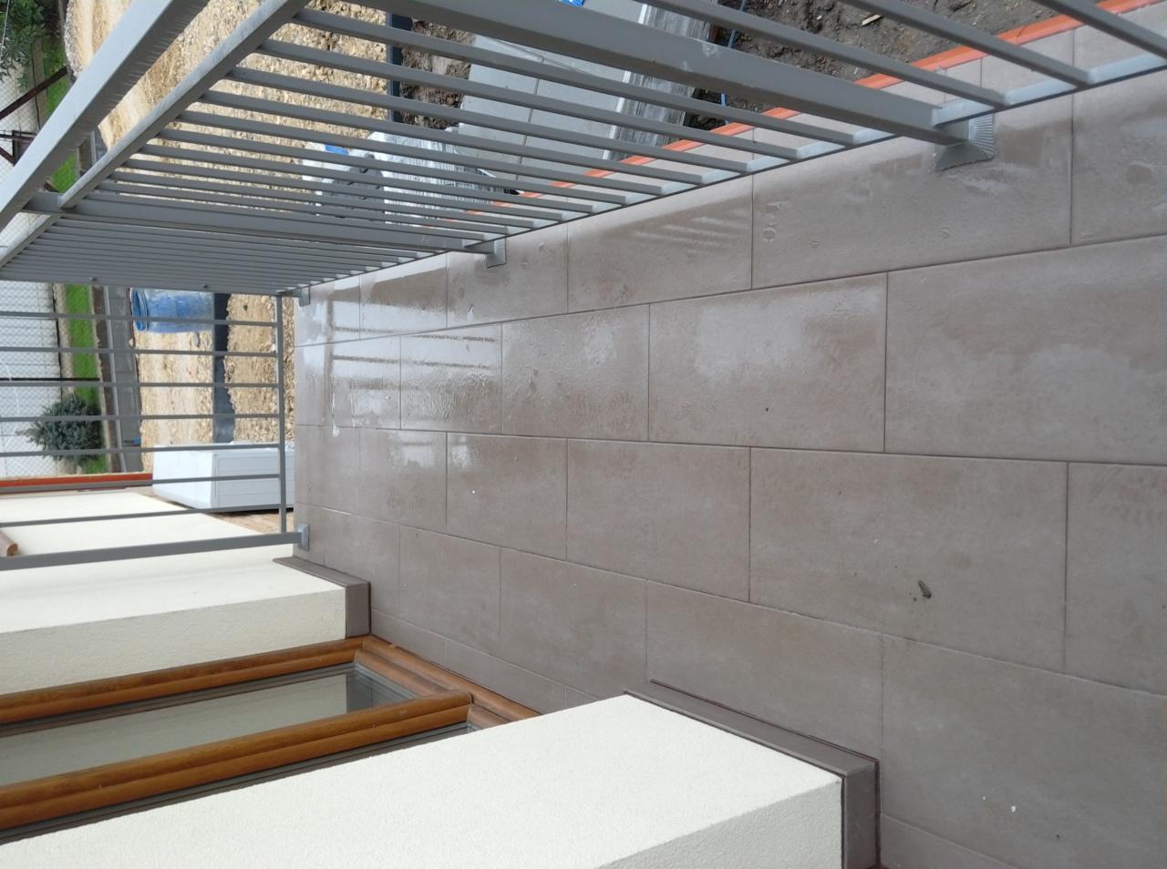 Świeżo ułożona, beżowa okładzina ceramiczna na ścianie zewnętrznej budynku w Mogilanach, widok z dołu na metalową konstrukcję zadaszenia.