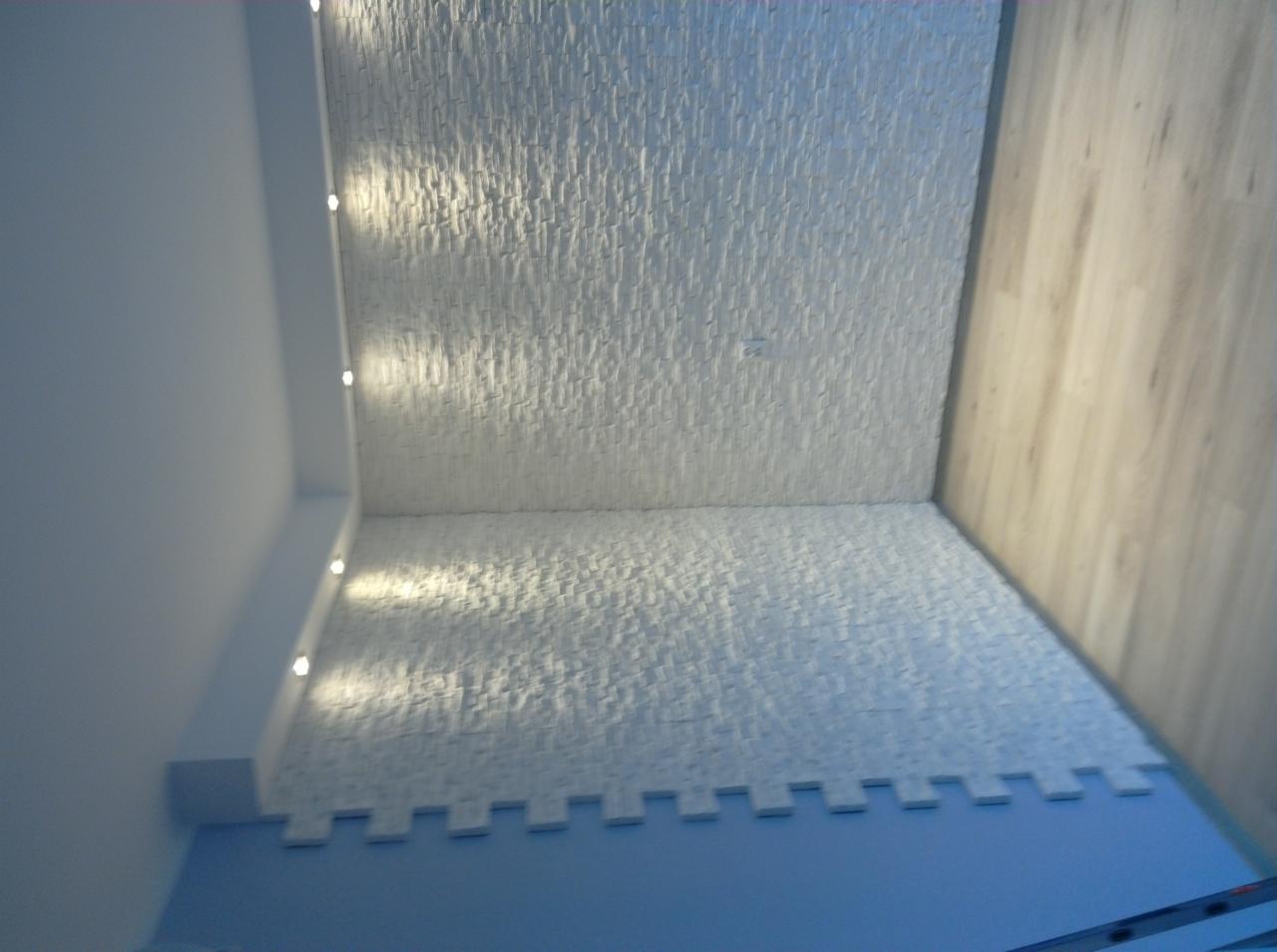 Wykończone wnętrze: ściany i sufit pokryte białą, strukturalną okładziną, oświetlenie punktowe w suficie, jasne panele na ścianie, widoczny fragment drabiny.