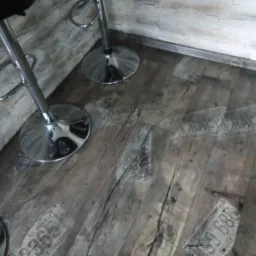 Ułożona podłoga z paneli imitujących stare drewno z nadrukiem numerów rejestracyjnych samochodów, widoczne chromowane nogi stołków barowych