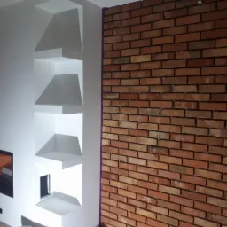 Ściana z cegły klinkierowej sąsiadująca z białą ścianą z wnękami, zabezpieczona taśmą malarską na łączeniu.