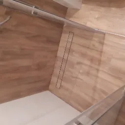 Nowoczesna kabina prysznicowa z odpływem liniowym w posadzce, wykończona płytkami imitującymi drewno.