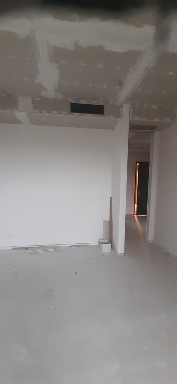 Wnętrze w trakcie remontu: sufit z płyt gipsowo-kartonowych z widocznymi łączeniami do szpachlowania, gładkie ściany przygotowane do malowania, surowa podłoga, widoczne przewody wentylacyjne...