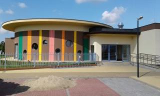 Nowoczesny budynek użyteczności publicznej w Górnie, z okrągłą częścią elewacji w pionowe pasy w kolorach brązowym, żółtym, zielonym i pomarańczowym, z okrągłymi oknami, ogrodzony niskim, metalowym...