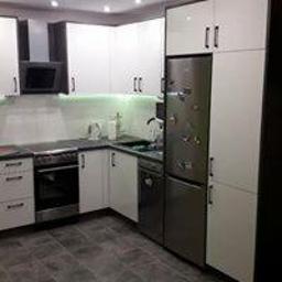 Meble na wymiar - Nowoczesna kuchnia z białymi frontami szafek, czarnymi akcentami, stalową lodówką i szarą podłogą z płytek. Oświetlenie LED pod szafkami górnymi.