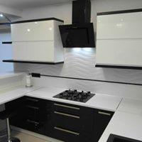 Nowoczesna kuchnia z białymi górnymi szafkami z czarnymi obramowaniami i czarnymi dolnymi szafkami z białym blatem, czarny okap nad płytą gazową.