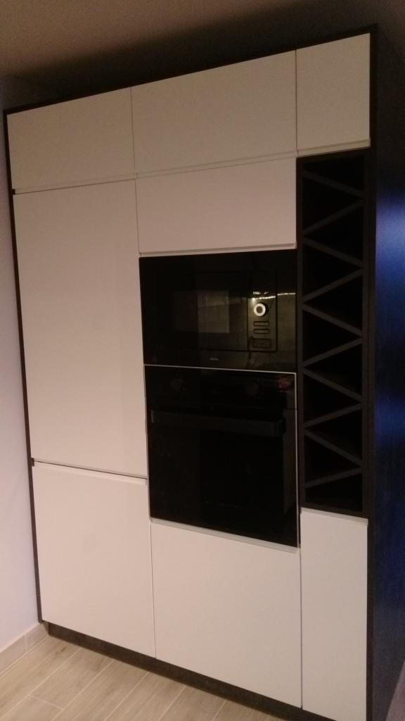 Biała zabudowa kuchenna z czarnymi piekarnikiem i mikrofalówką oraz wstawką na wino z ciemnego drewna.