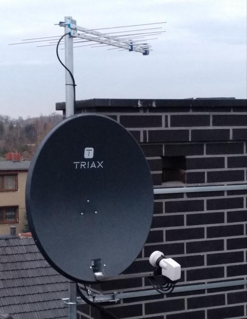 Antena satelitarna Triax i antena kierunkowa UHF zamontowane na kominie z ciemnej cegły, widok z dołu na tle szarego nieba.