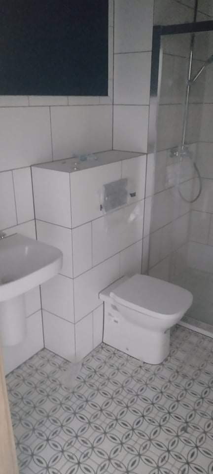 Nowoczesna, wykafelkowana łazienka z wiszącą miską WC, umywalką na postumencie i kabiną prysznicową, wykończona płytkami podłogowymi w geometryczny wzór.