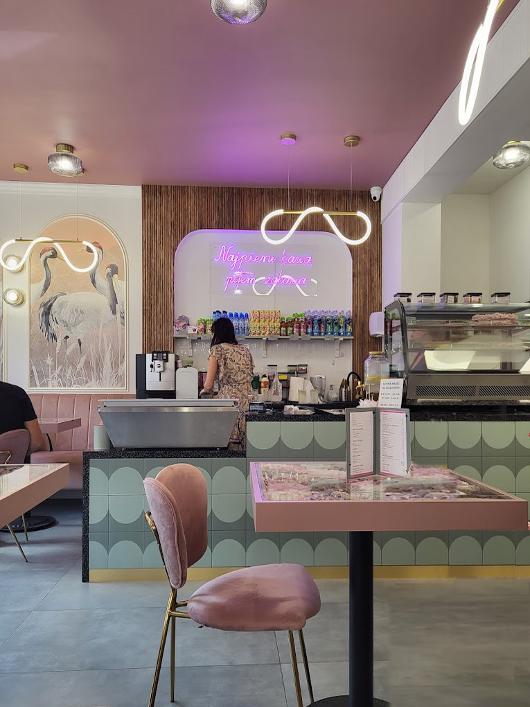 Wnętrze kawiarni w Wejherowie z różowym sufitem, neonowym napisem 'Najpierw kawa, potem zabawa', pastelowymi meblami i dekoracjami w stylu retro.