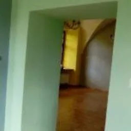 Świeżo pomalowane, jasnozielone ściany w przejściu między pokojami, widoczne łuki i drewniana podłoga, okno z żółtą zasłoną w tle.