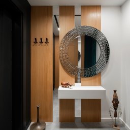 Wnętrze przedpokoju z niestandardową jasną podłogą i drewnianymi ścianami tworzy przytulną atmosferę. Lustra w formie dekoracji dodają elegancji i optycznie powiększają przestrzeń, wprowadzając światło do wnętrza.