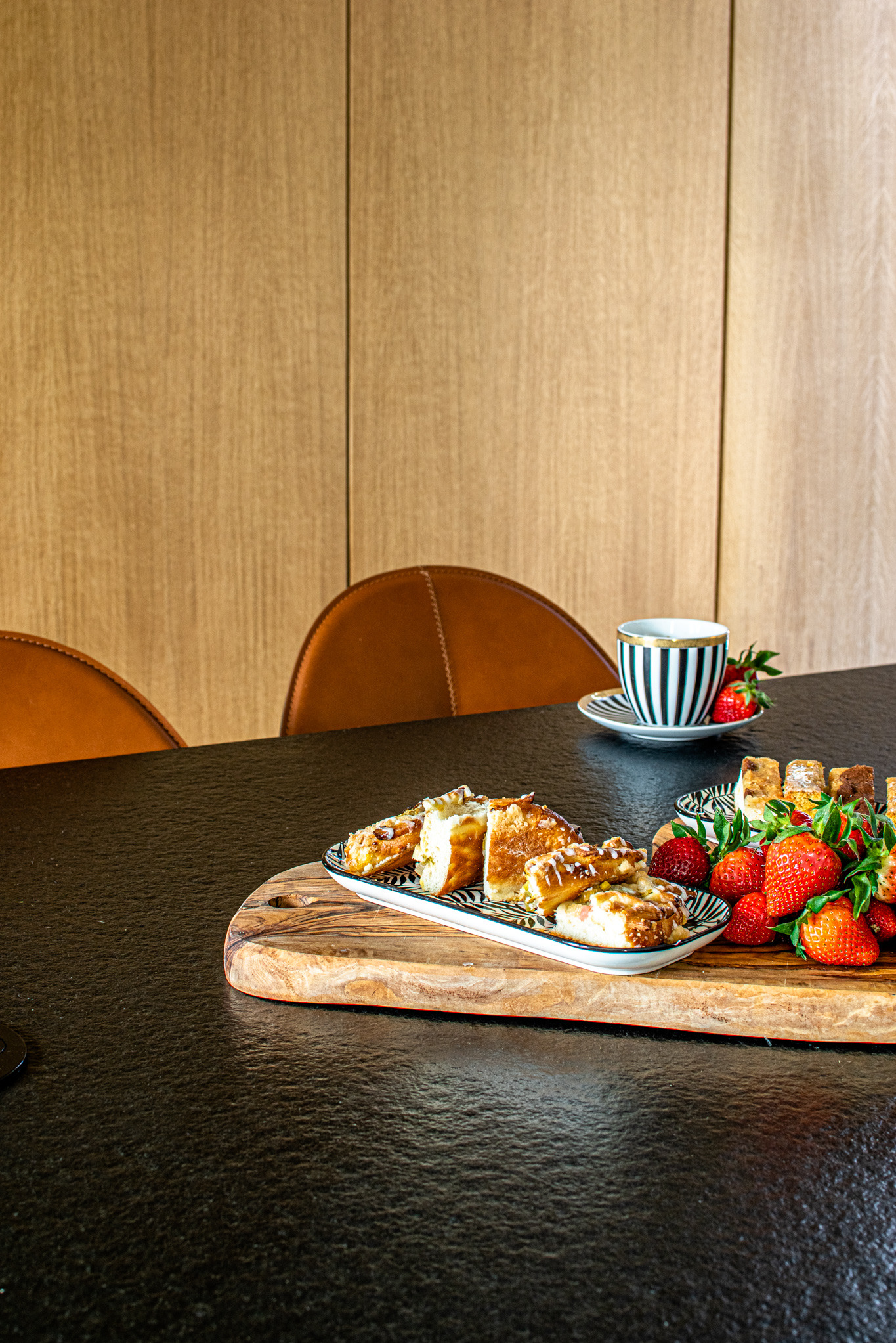 Deser z truskawkami na drewnianej desce, czarno-biała filiżanka i skórzane krzesła w tle, aranżacja stołu w neutralnej kolorystyce.