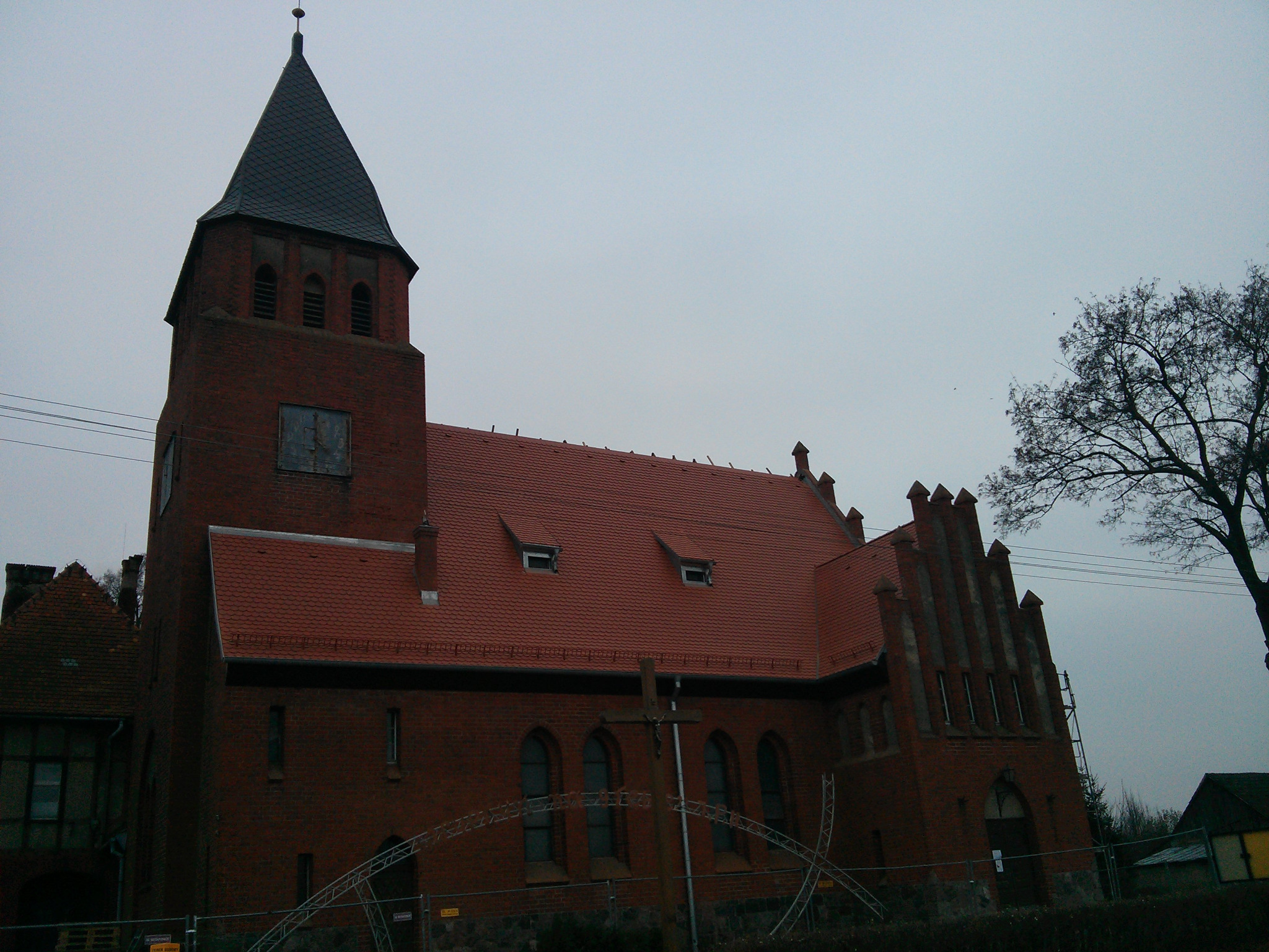 Ceglany kościół z czerwoną dachówką w Obornikach, z widoczną wieżą i elementami rusztowania przed budynkiem.