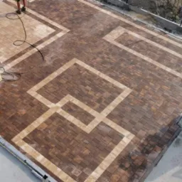 Widok z góry na nowo ułożony wzór z brązowej i beżowej kostki na posesji, paleta z kostką i narzędzia w tle.