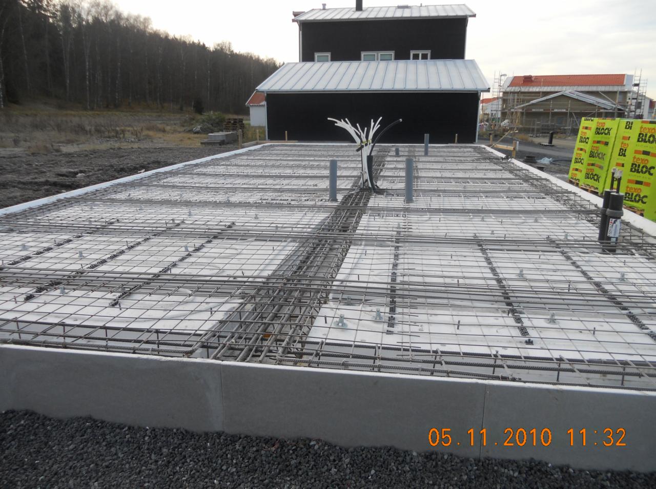 Zbrojenie fundamentu płyty betonowej z wystającymi rurami instalacyjnymi przed wylaniem betonu, widoczne bloczki styropianowe Texo Block.