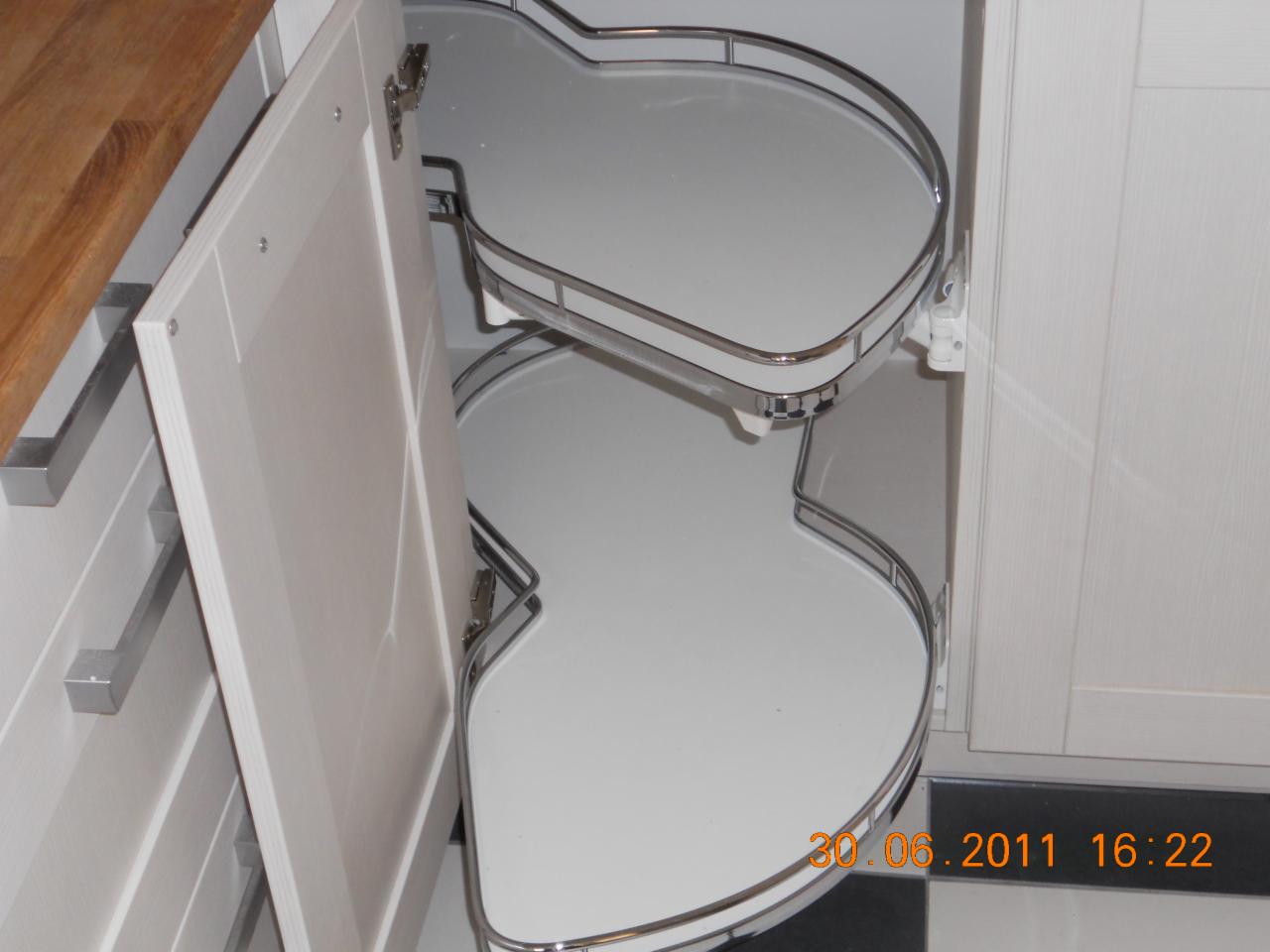 Wysuwana, dwupoziomowa półka narożna w szafce kuchennej z otwartymi drzwiczkami, widoczne metalowe elementy konstrukcyjne i białe półki.