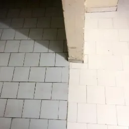 Białe kwadratowe płytki podłogowe, część wyczyszczona, część zabrudzona, z kolumną w rogu.