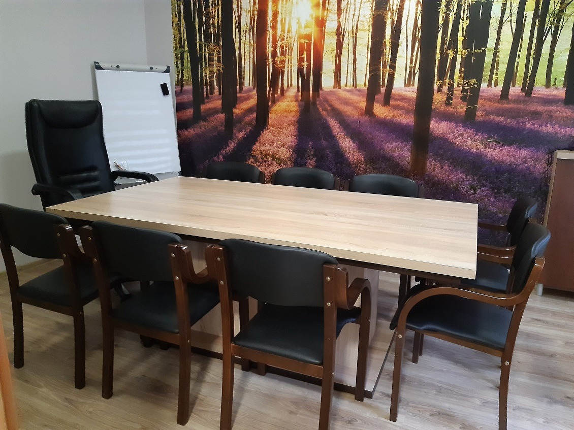 Sala konferencyjna z dużym stołem, krzesłami z czarnej skóry i fototapetą przedstawiającą las w tle.
