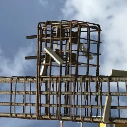 Zbrojenie kolumny żelbetowej z dystansami w trakcie montażu we Wrocławiu, na tle błękitnego nieba z chmurami.