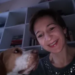 Uśmiechnięta kobieta robi selfie z psem rasy beagle na tle regału z książkami w domowym biurze.