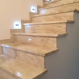 Wykończone schody wewnętrzne z trawertynu z podświetleniem LED, widok z dołu, ukazujący naturalny wzór kamienia i delikatne światło.