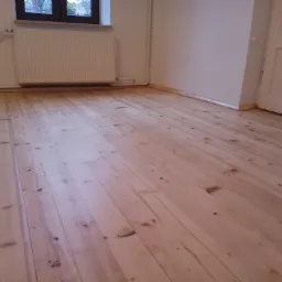 Jasna, odnowiona podłoga z desek w pustym pokoju z białymi ścianami, grzejnikiem i oknem.