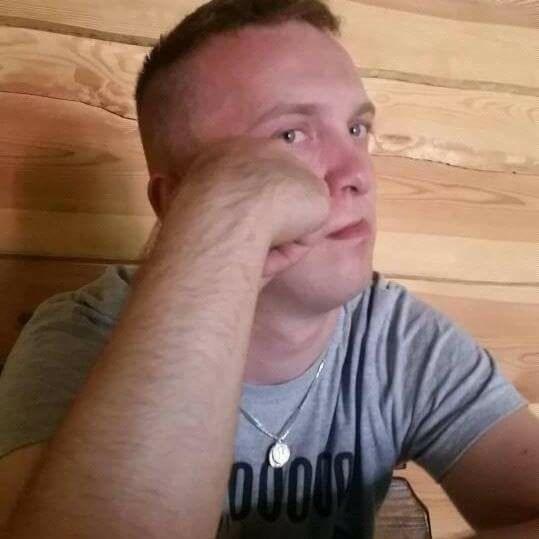 Mężczyzna z krótkimi włosami, oparty na ręce, zamyślony, na tle boazerii.